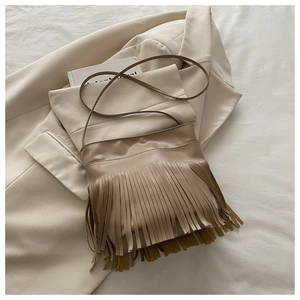 Detail of khaki tassel shoulder bag with bohemian fringe on soft cream blazer background