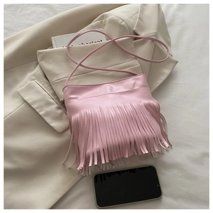 Detail shot of a pink fringe crossbody bag with long tassels on a beige blazer jacket