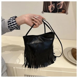 Detail of the black synthetic leather bucket bag with dense vertical tassels and long strap