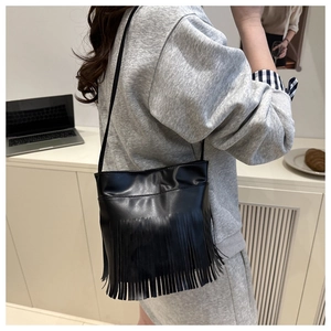 Detail of a black leather crossbody bag with long fringes and vintage ethnic style