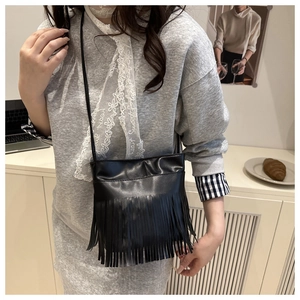 Detail shot of a black tassel crossbody bag in a cozy lifestyle coffee shop setting