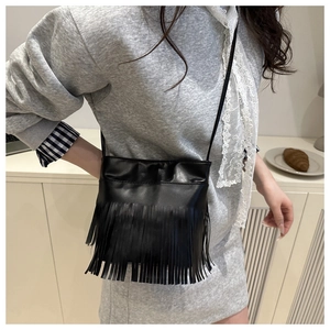Detail of a chic black faux leather crossbody bag with long fringe tassels on a model
