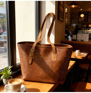 Brown leather tote bag featuring a gold fashion logo on a wooden cafe windowsill