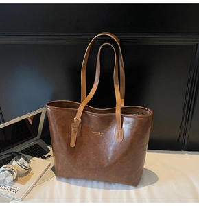 Close-up of retro brown leather tote bag with gold lettering and metal buckle details