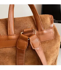 Détail d'un sac à dos en daim marron montrant les coutures renforcées et l'anneau en D