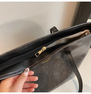 Detailed close-up of smooth metal zipper and premium leather texture of black tote bag