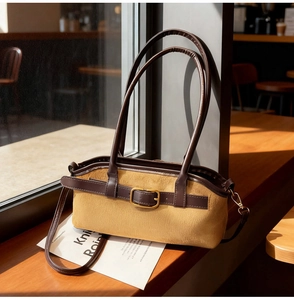 Vue détaillée du sac bandoulière en daim marron avec boucle dorée sur un rebord de fenêtre
