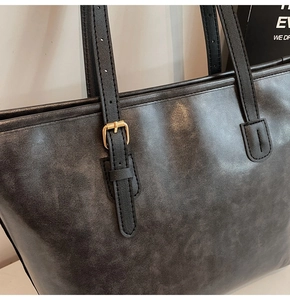 Detail of dark grey tote bag featuring vintage leather texture and gold metal buckle