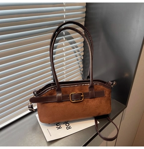 Détail d'un sac à bandoulière en daim marron foncé avec boucle dorée sur rebord de fenêtre