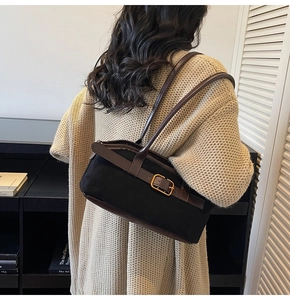 Détail du sac à bandoulière en toile noire avec garniture en cuir brun et boucle dorée