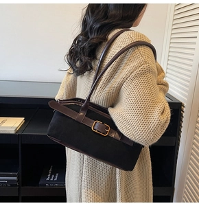 Détail d'un sac à bandoulière en daim noir avec sangle en cuir marron sur un pull beige