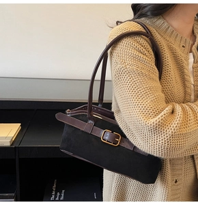 Détail du sac bandoulière en daim noir avec lanière en cuir marron et boucle dorée