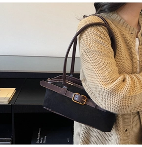 Détail d'un sac bandoulière en daim noir avec lanière en cuir marron et boucle dorée