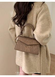 Detail of a brown textured crossbody bag styled with a beige coat in a retro setting