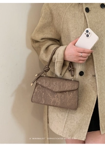 Detail of brown striped texture handbag with decorative knotted handle and gold metal rings