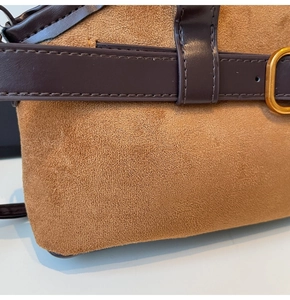 Détail montrant la texture du daim marron et la bandoulière en cuir avec boucle dorée du sac