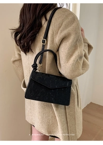 Detail view of black corduroy shoulder bag with knot handle on model in wool coat