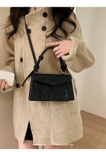 Minimalist black textured crossbody bag with unique knot handles and golden hardware detail