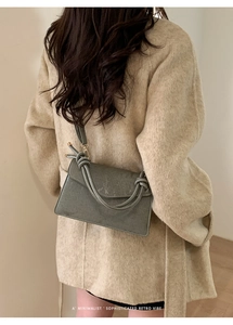 Close-up of a retro sage green leather crossbody bag with a unique knot handle detail