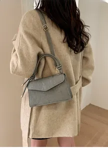 Close-up of a blue-gray crossbody bag with fine ribbed texture on a beige coat