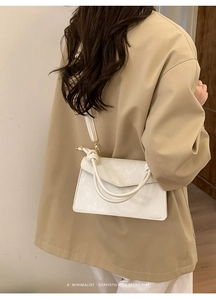Detail of white minimalist crossbody bag with dual knotted handles and polished leather texture