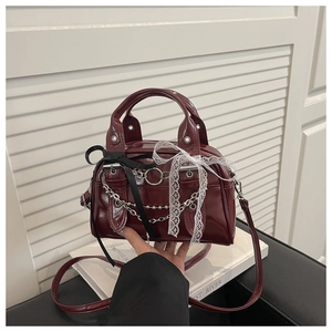 Detail of burgundy patent leather bag with lace bow and silver chain decoration
