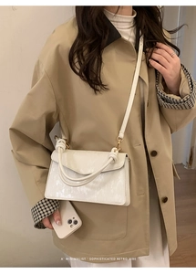 Detail of white wave-flap crossbody bag with twisted handle and pearlescent texture