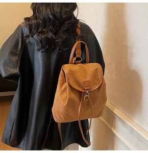 Close-up of brown suede backpack with leather trim worn over a black jacket