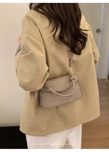 Detail of grey textured crossbody bag with unique knot handle shown on a model