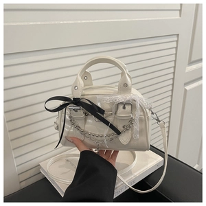 Detail of cream patent leather mini bag with lace trim, black bow, and silver cross charm