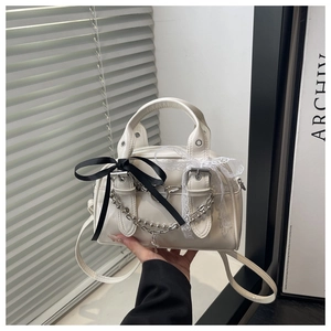 Close-up of cream crossbody bag featuring lace and satin bow detailing with metal chains