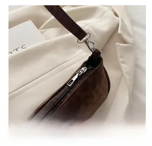 Detailed close-up of a smooth silver zipper on a brown suede crossbody bag with TC card