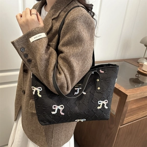 Quilted tote bag with embroidered bows and shoulder strap shown on a model