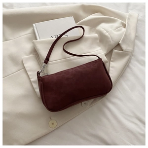 Détail du sac baguette en daim bordeaux avec ferrures argentées sur une veste blanche