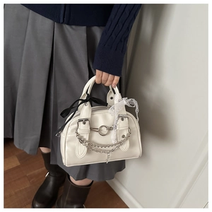 Close-up of white leather handbag with silver chains, lace ribbons, and black satin bow