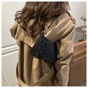 Close-up of black leopard print bag with silver hooks worn on a beige trench coat