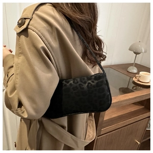 Detail of black leopard print baguette bag on a shoulder, styled with a camel trench coat
