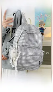 Detail of checkered canvas backpack with white fuzzy ball charm and brand side label