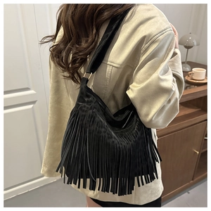 Detail of black suede shoulder bag featuring bohemian fringe and wide strap on model