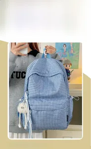 Blue plaid canvas backpack with a cute white plush pendant shown in hand detail