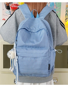 Detailed back view of a blue plaid backpack with a cute fuzzy monster keychain charm
