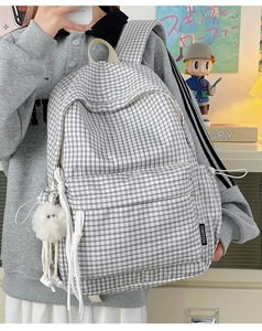 Close-up of black and white plaid backpack with plush charm and side brand label detail