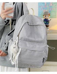 Side view of black and white plaid canvas backpack with a white plush monster keychain