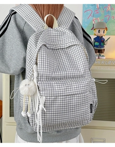 Detail of vintage plaid backpack showing side pocket and white fluffy pompom pendant