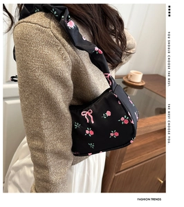 Detail view of black underarm bag featuring pink ribbon bow and floral prints on fabric