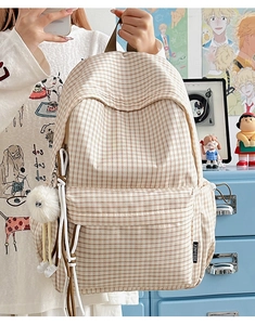 Detail of vintage plaid backpack showing XINFEIDA side label and plush ball accessory