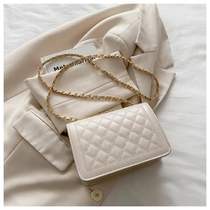 Detail of beige quilted flap crossbody bag with golden chain strap on suit jacket
