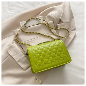 Detail of green quilted crossbody bag with gold chain strap on a beige blazer background