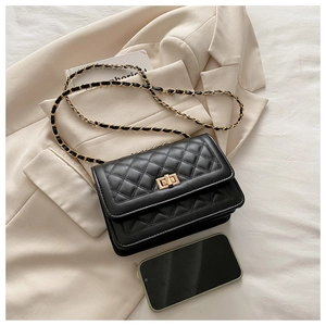Top view of black quilted crossbody bag with gold lock and chain on beige blazer