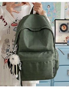Detail of green plaid backpack featuring a fuzzy monster charm and spacious front pocket